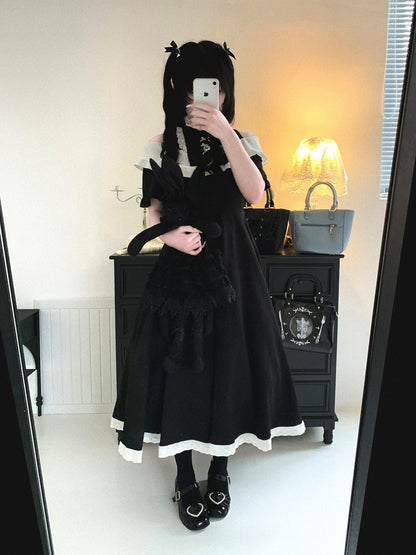 Person wearing a black and white outfit with a large black cat plushie in a room.
