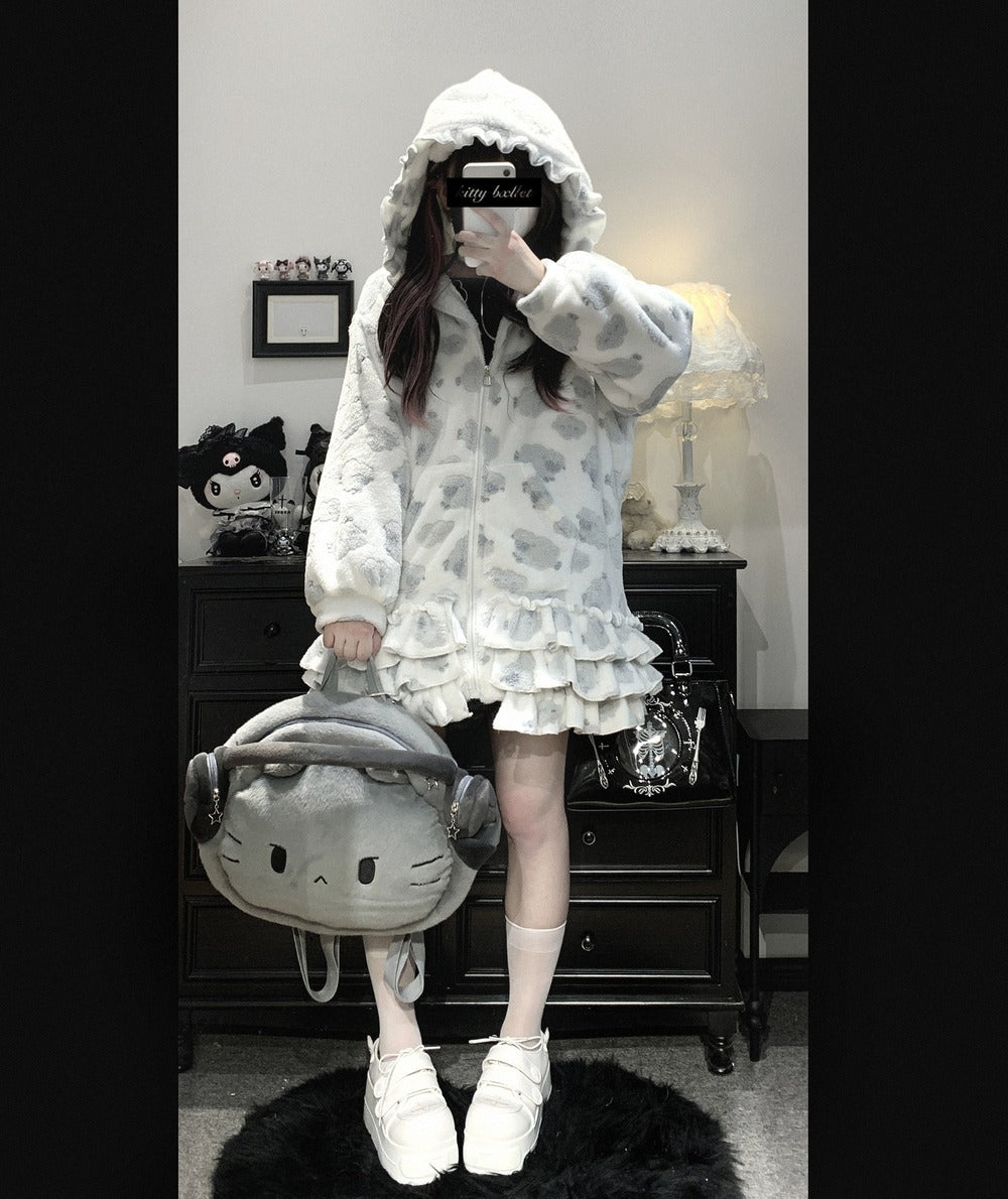 Person wearing a white hooded outfit with ruffles, holding a gray backpack with a cat design, in a room.