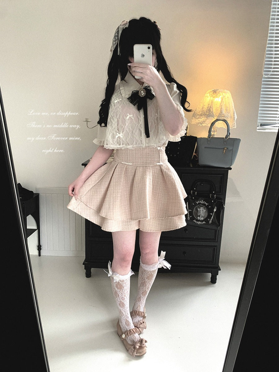 Person wearing a white lace top and beige pleated skirt in a room.