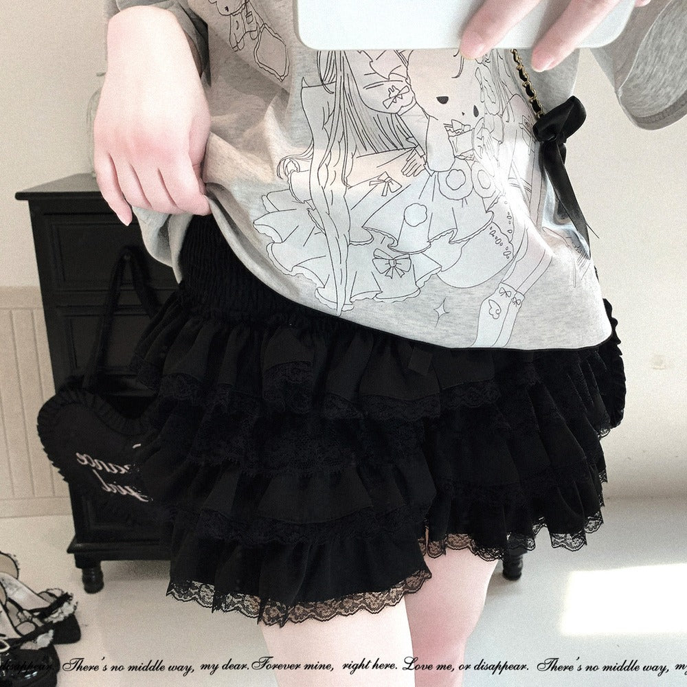 A person wearing a black tiered ruffle skirt with lace trim and a light gray graphic t-shirt, standing in an indoor setting next to a dark wooden cabinet.