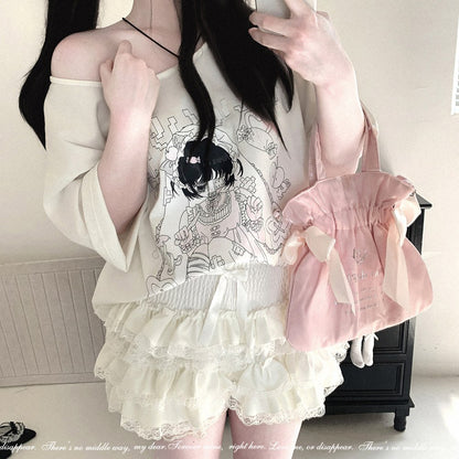 A person takes a mirror selfie wearing a cream off-the-shoulder top with a black anime-style graphic, matching cream ruffled shorts, and carrying a light pink drawstring bag with a large ribbon bow.