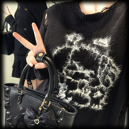 Person wearing a black sweater with white abstract design, holding a black handbag.
