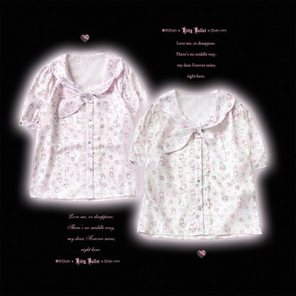 Two short-sleeve button-front blouse tops with a ruffled collar and bow detail, shown on a black background. The left top is light pink with a subtle floral print, and the right top is white with a similar light pink floral print.
