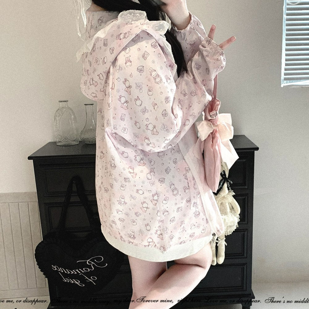 A person wearing a light pink hooded jacket with a delicate cartoon print, posing in front of a dark wooden cabinet in an indoor setting.