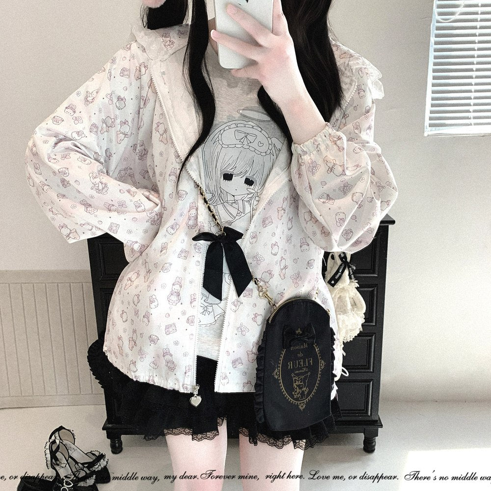 A person taking a mirror selfie wearing a white long-sleeve hooded jacket with a delicate pink and gray cartoon pattern, a black ribbon bow at the waist, a black lace skirt, and a black crossbody bag with gold lettering.