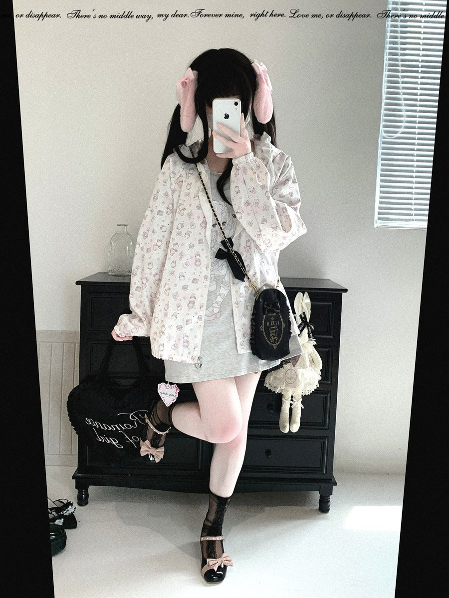 A person taking a mirror selfie wearing a light pink and white floral print oversized cardigan, a light gray mini skirt, and black lace-up heels, with a black crossbody bag and a small white plush toy hanging from the bag.