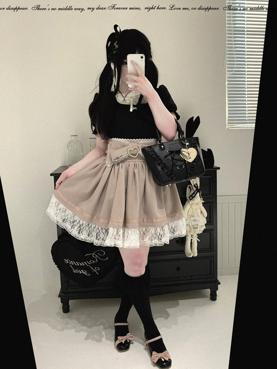 A person takes a mirror selfie in a room, wearing a black top and skirt with a beige pleated skirt featuring white lace trim, black knee-high socks, and black shoes. They are holding a black handbag with a gold heart detail.