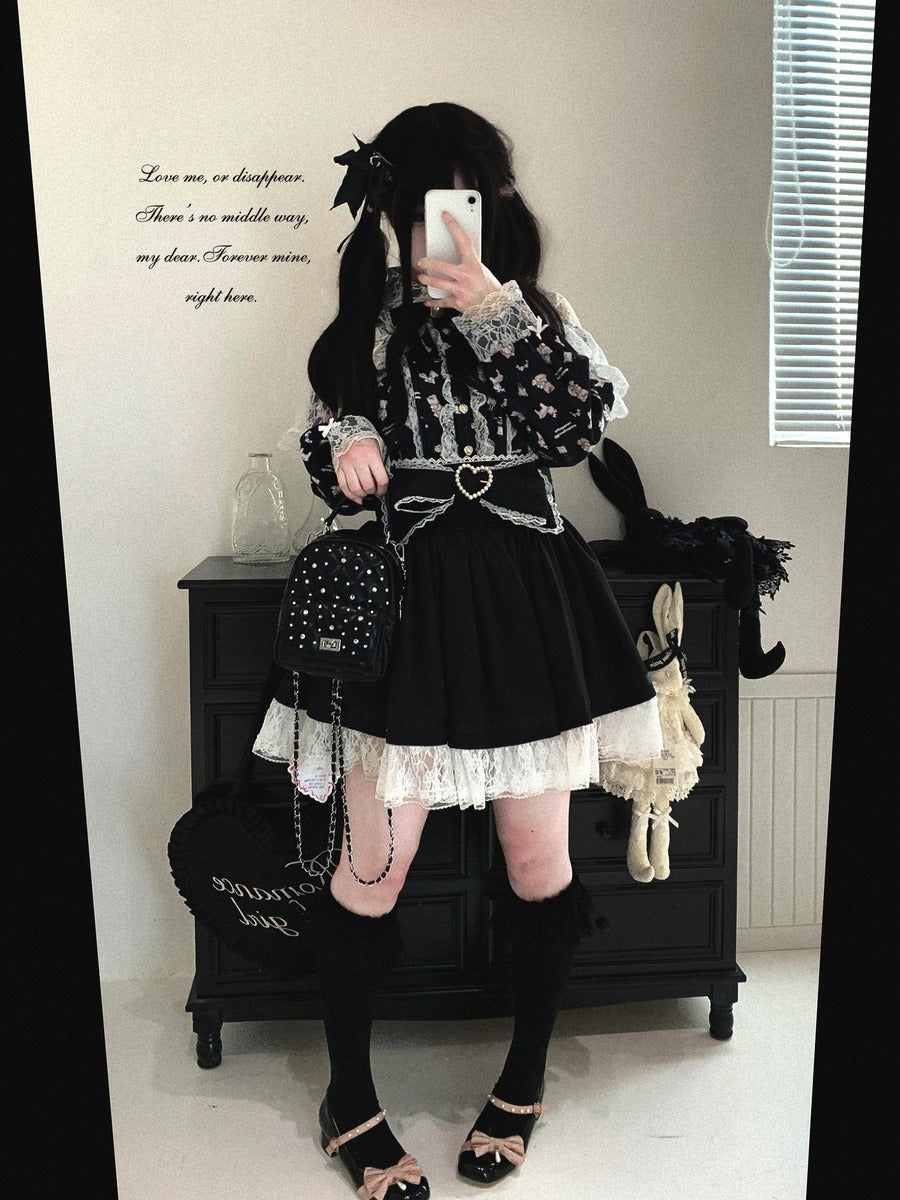 A person takes a mirror selfie wearing a black and white gothic Lolita-style outfit with a lace-trimmed top, pleated black skirt, heart-shaped belt, knee-high socks, and bow shoes. The setting is an indoor room with a dark wooden cabinet, wall text, and window blinds.