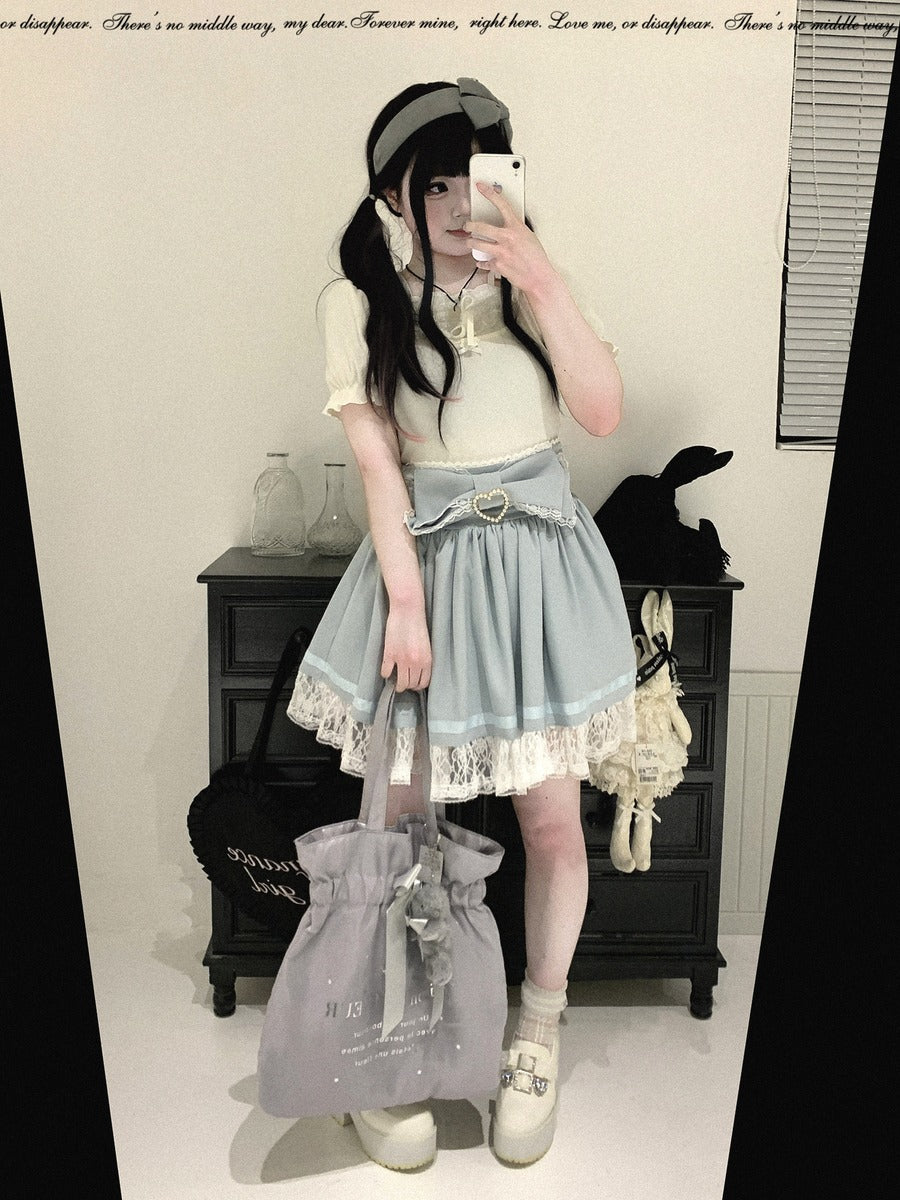 A person takes a mirror selfie wearing a light blue and white Lolita-style dress with a pleated skirt, lace hem, and a matching headband. They are holding a large lavender-gray drawstring tote bag in a room with a dark cabinet and decorative items.