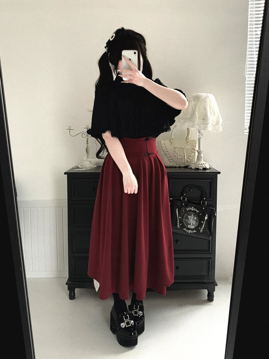 Person wearing a black top and red skirt taking a mirror selfie in a room with a black dresser.
