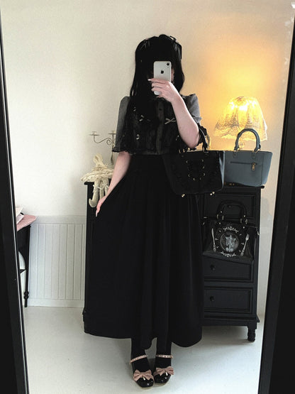 Person wearing a black outfit with a skirt, standing in front of a mirror.