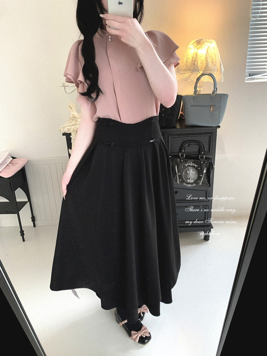 Person wearing a pink top and black skirt in a room with a dresser and lamp.