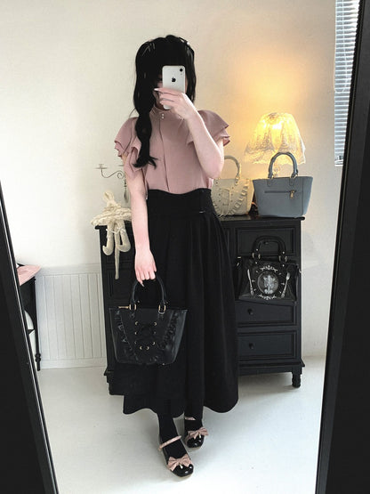 Person wearing a pink top and black skirt with a handbag, standing in front of a mirror.
