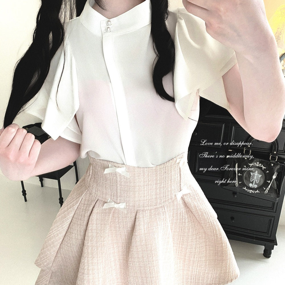 A person wearing a cream short-sleeve blouse with a high collar and pleated skirt in a light beige tweed fabric, shown in a mirror selfie.