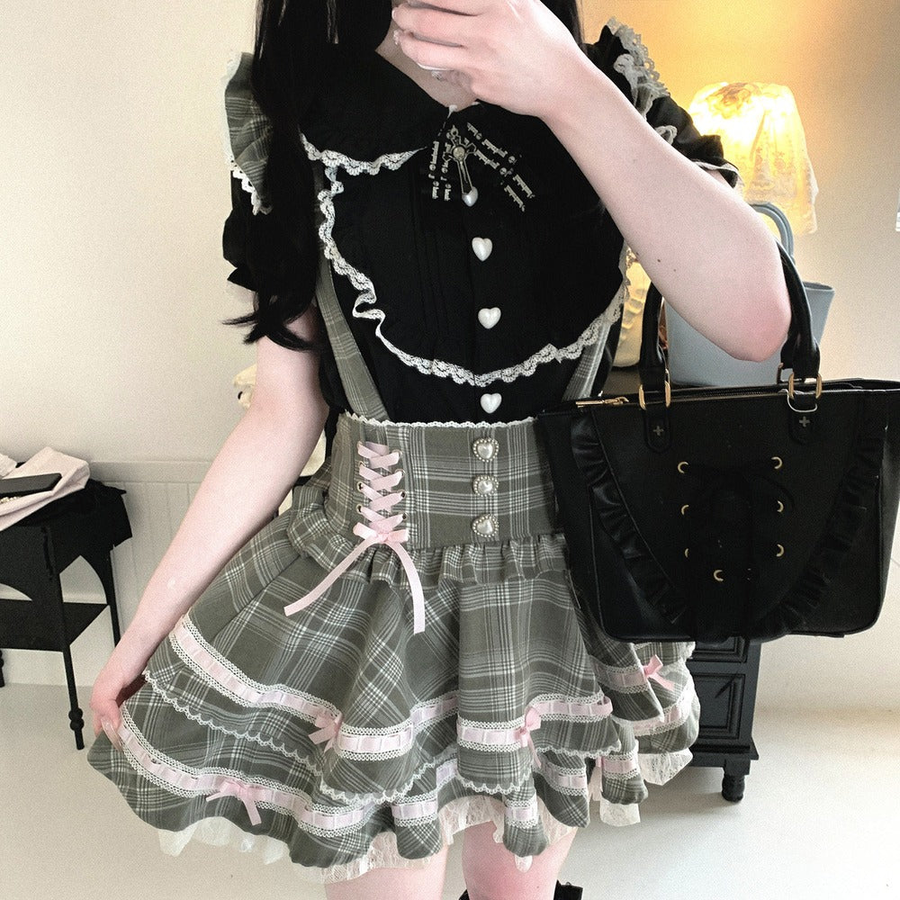 Person wearing a black top with white heart details and a plaid skirt, holding a black handbag.