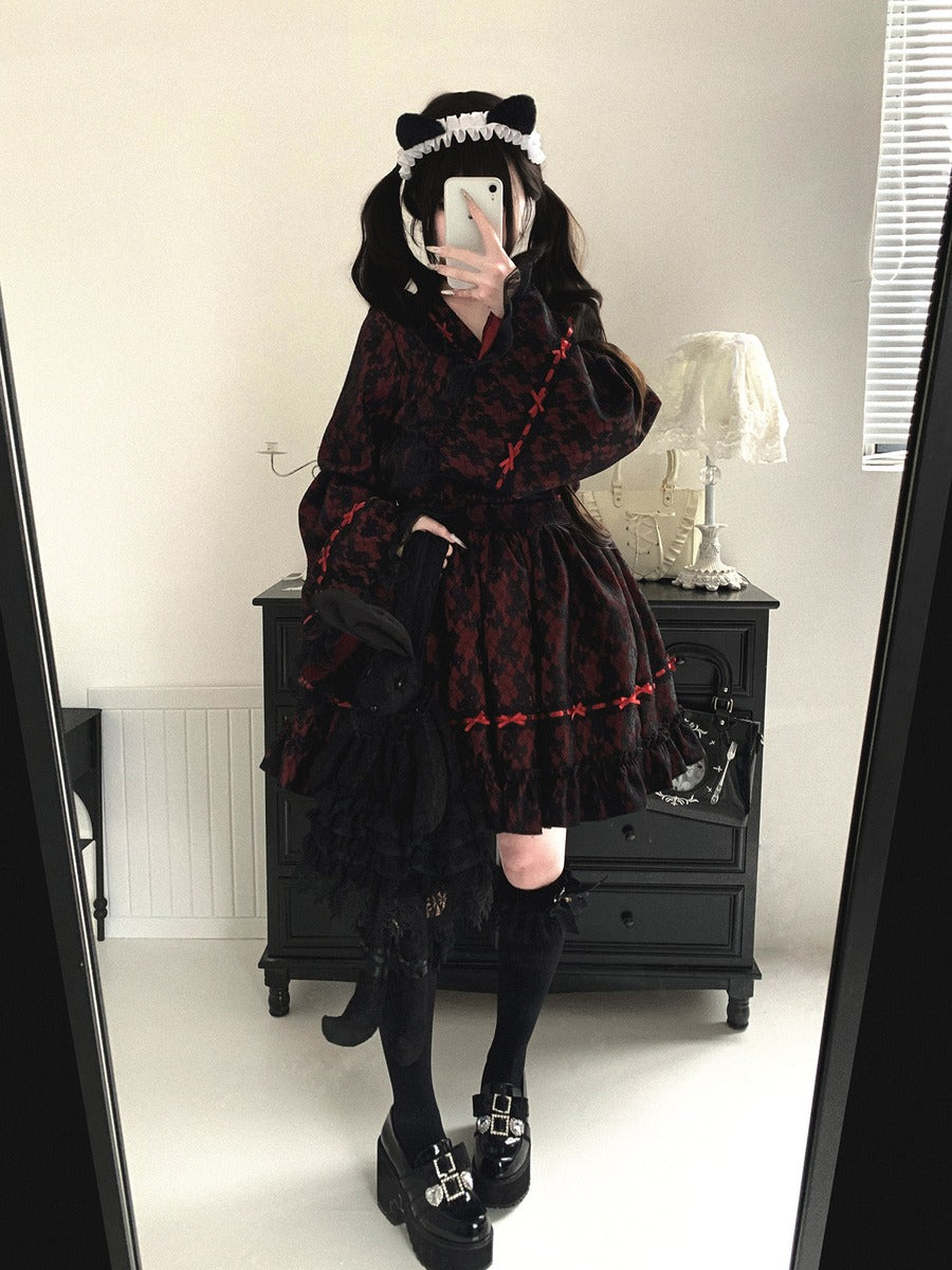Person wearing a dark kimono plaid dress with a hood in a room.