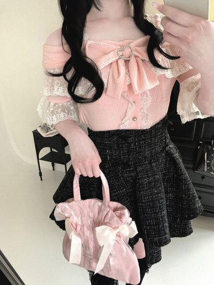 Person wearing a pink top with a bow and black skirt, holding a pink bag.