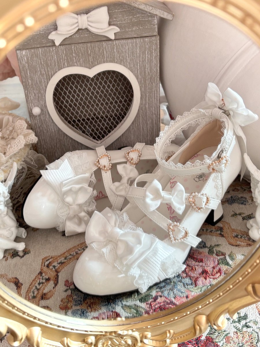 White lace-up shoes with decorative bows and pearls on a floral-patterned surface.