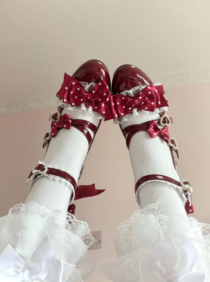 Red polka dot shoes with bows and white stockings on a light pink background