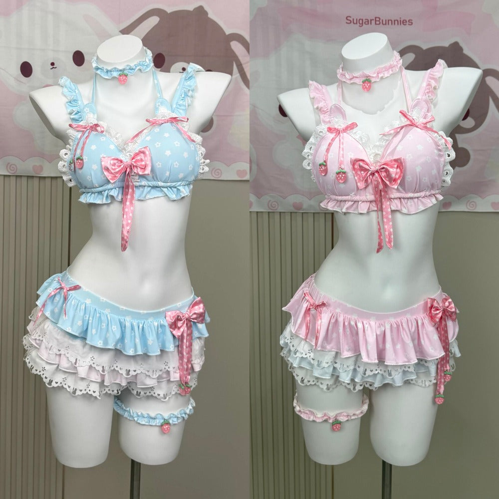 Two pastel anime-style lingerie sets displayed on white mannequins, featuring a light blue and white polka-dot bra top with pink bow and strawberry details, paired with matching ruffled bottoms and choker/leg bands. The right set is light pink and white with pink bows.