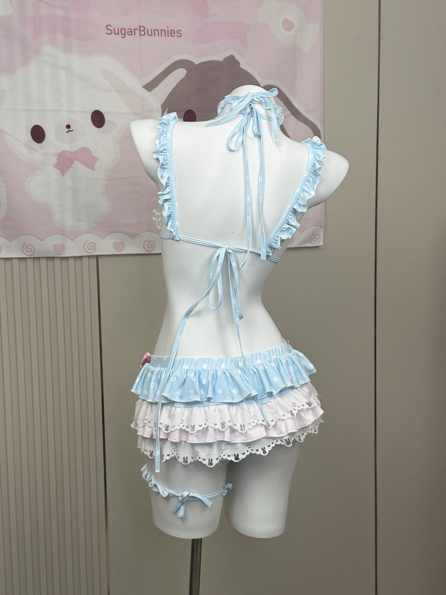 A light blue and white ruffled lingerie-style outfit displayed on a white mannequin torso, with matching leg straps. The background shows a beige wall and a pink Sanrio-themed poster.
