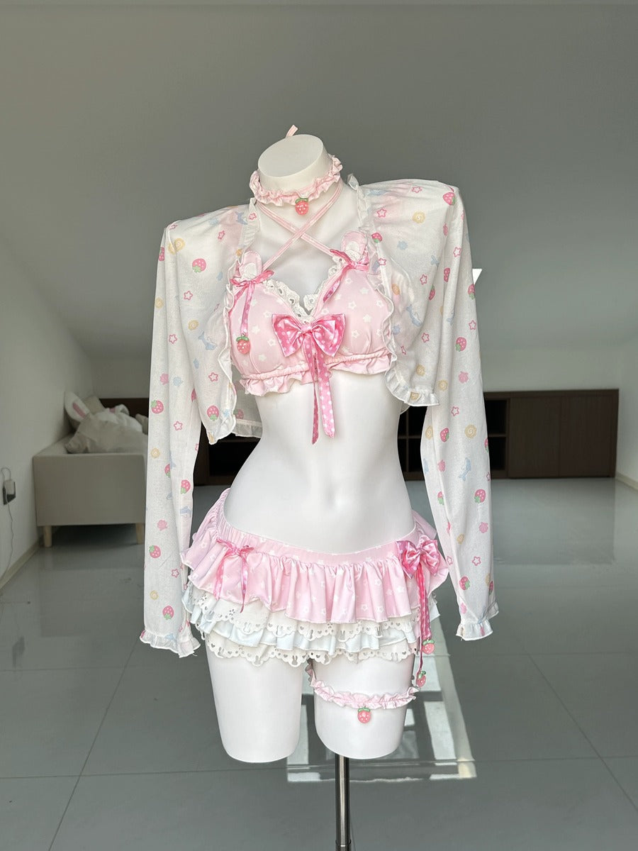A pink and white Lolita-style lingerie set displayed on a white mannequin torso in a room. The set includes a long-sleeve white crop top with pink floral patterns, a pink ruffled bralette with a large bow, matching ruffled shorts, and a pink choker.