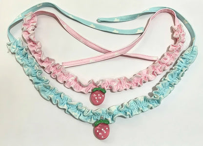 A pastel pink and light blue ruffled collar with two small strawberry charms hanging from the center, displayed on a plain white background.