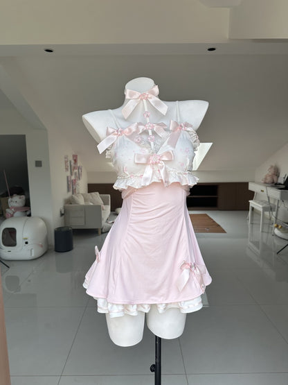 A light pink and white Lolita-style dress displayed on a white mannequin torso in a modern home interior. The dress features a ruffled halter-style top with multiple pink bows, a pleated skirt, and white ruffle trim.