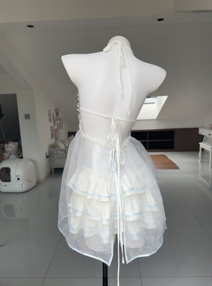 White tiered ruffled dress displayed on a white mannequin torso in a bright indoor room with tiled floors and slanted ceiling windows.