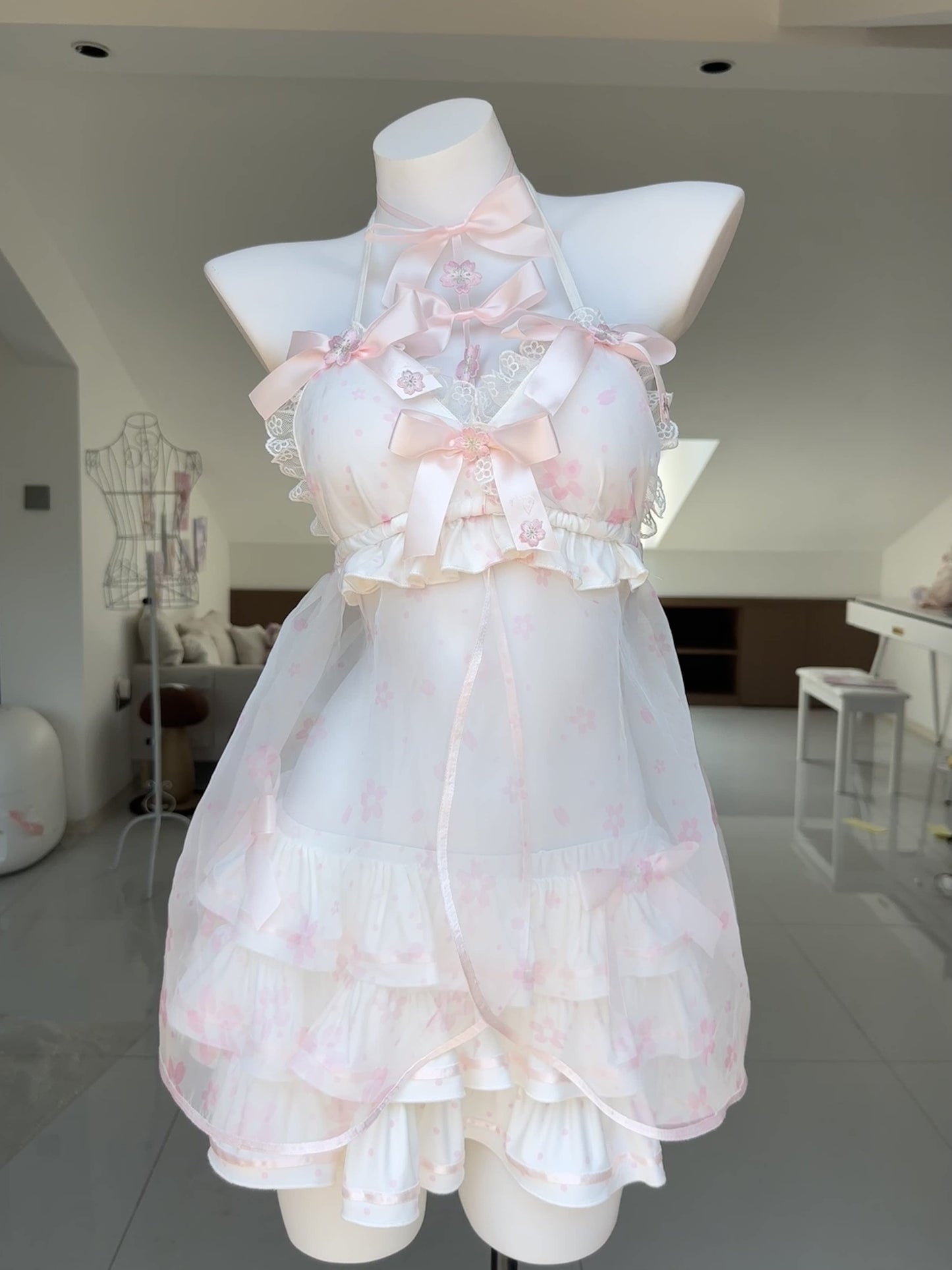 A white and pale pink halter babydoll dress with ruffles and bows, displayed on a white mannequin in a bright indoor room.
