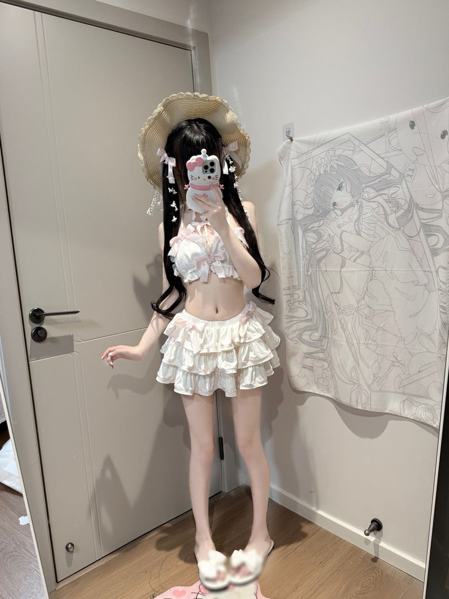 A person taking a mirror selfie indoors wearing a white ruffled two-piece outfit with a matching wide-brim straw hat. The room has a beige door, wood floor, and a large anime-style tapestry hanging on the wall.