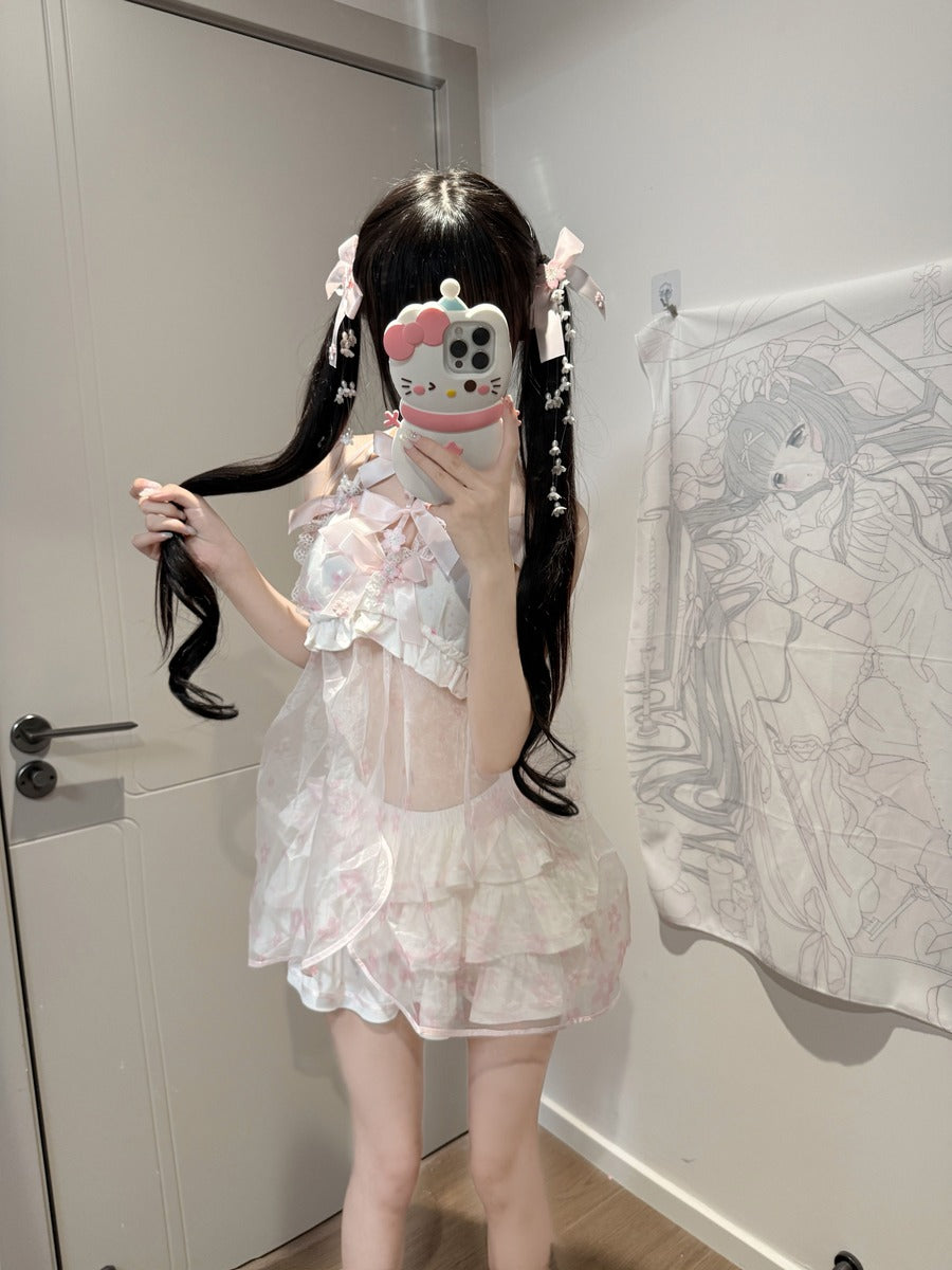 A person taking a mirror selfie in a room, wearing a short, sheer white and pink ruffled dress with a high back. The room has a white door on the left and a white wall with an anime print hanging on the right.