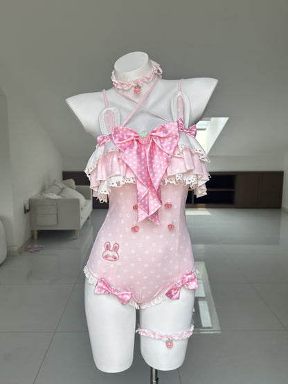A pink Lolita-style bodysuit with white polka dots, ruffled trim, a large bow at the chest, and matching accessories including a choker, garter belt, and thigh strap, displayed on a white mannequin in a bright room.