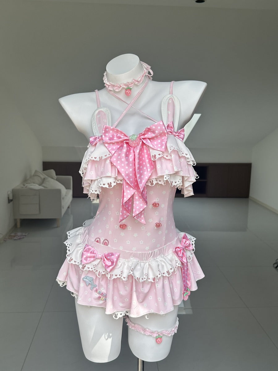 A pink and white Lolita-style ruffled romper displayed on a white mannequin torso in a minimalist indoor room. The outfit features multiple layers of ruffles, large bows, lace trim, and small embroidered details.