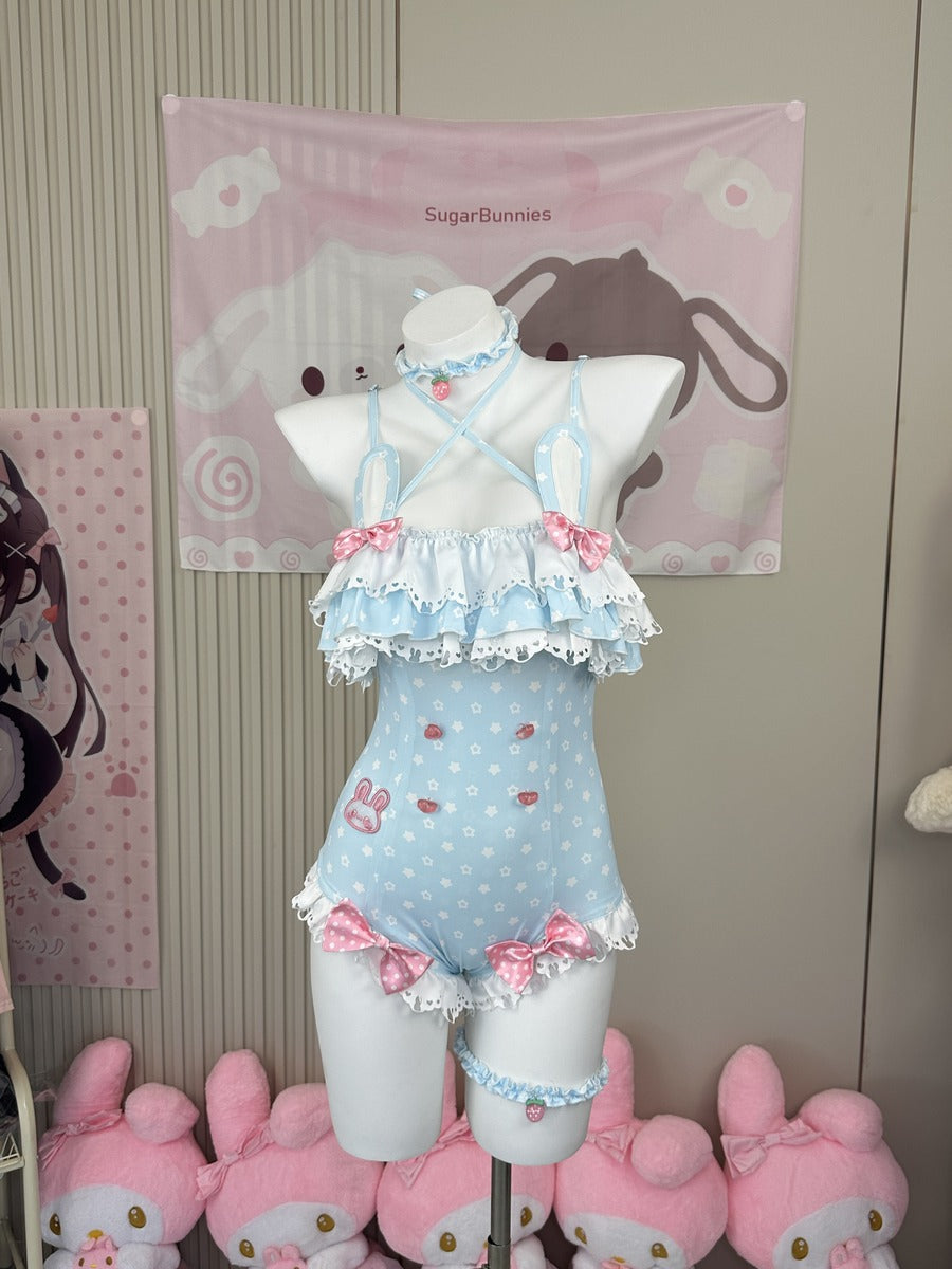 A light blue and white polka dot ruffled one-piece swimsuit with pink bows, displayed on a white mannequin torso. The swimsuit features a halter-style top with lace trim, a polka dot bodice with small bunny and strawberry motifs, and ruffled trim at the legs.