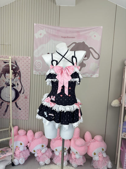 A black and pink polka-dot Lolita-style dress displayed on a white mannequin torso in a room decorated with anime-themed wall hangings and pink plush toys.