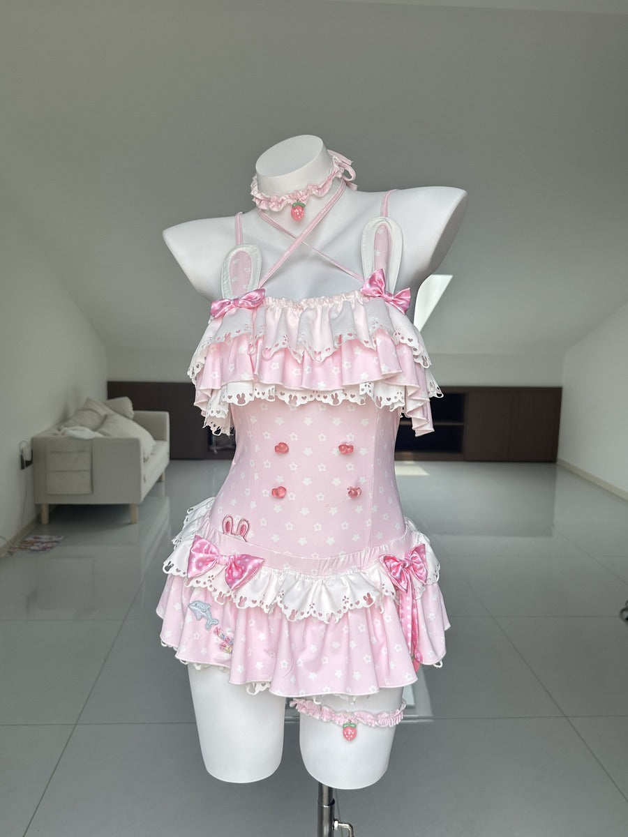 A pink Lolita-style mini dress with white lace trim, ruffles, and bow details, displayed on a white mannequin in a room with a tiled floor and slanted ceiling.
