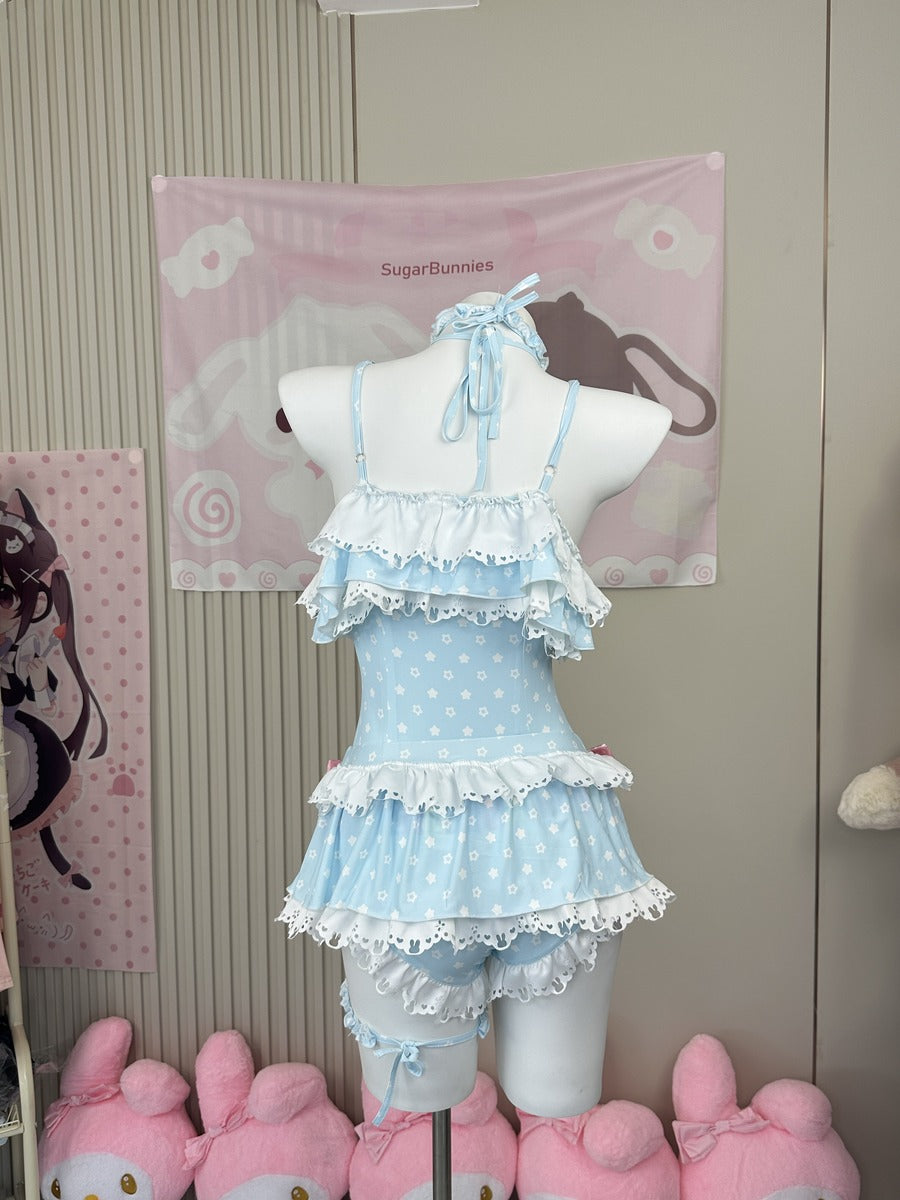 A light blue and white polka dot Lolita-style romper with layered ruffles and lace trim, displayed on a white mannequin torso. The background features a pink wall tapestry with cartoon graphics and pink plush toys at the bottom.