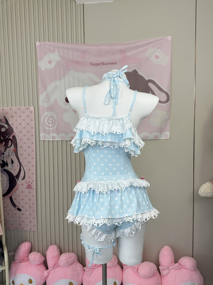 A light blue and white polka dot Lolita-style romper with layered ruffles and lace trim, displayed on a white mannequin torso. The background features a pink wall tapestry with cartoon graphics and pink plush toys at the bottom.