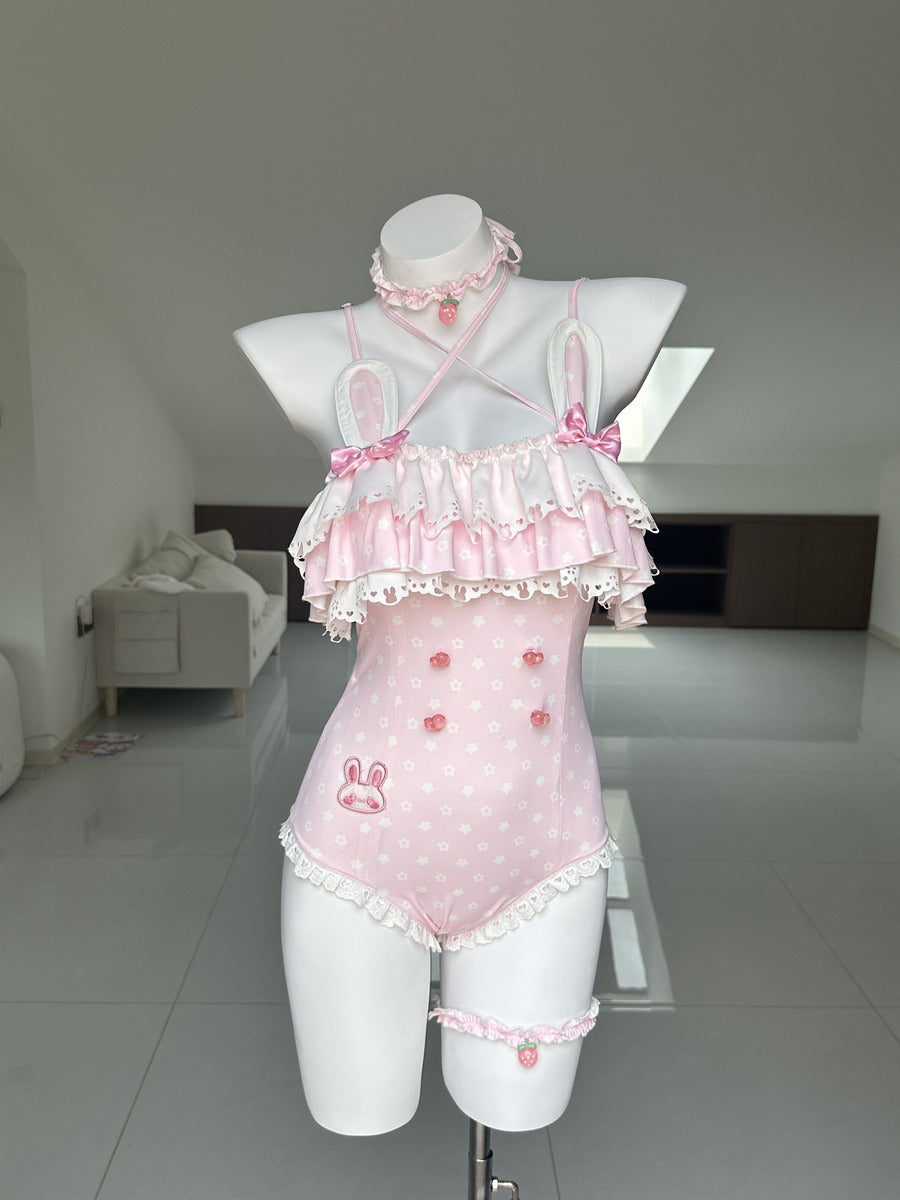 A pink bunny-themed lingerie set displayed on a white mannequin torso in a bright, modern room. The set includes a ruffled halter top with bunny ears, a polka-dot bodysuit with bunny motifs, a matching choker, and garter-style leg bands.
