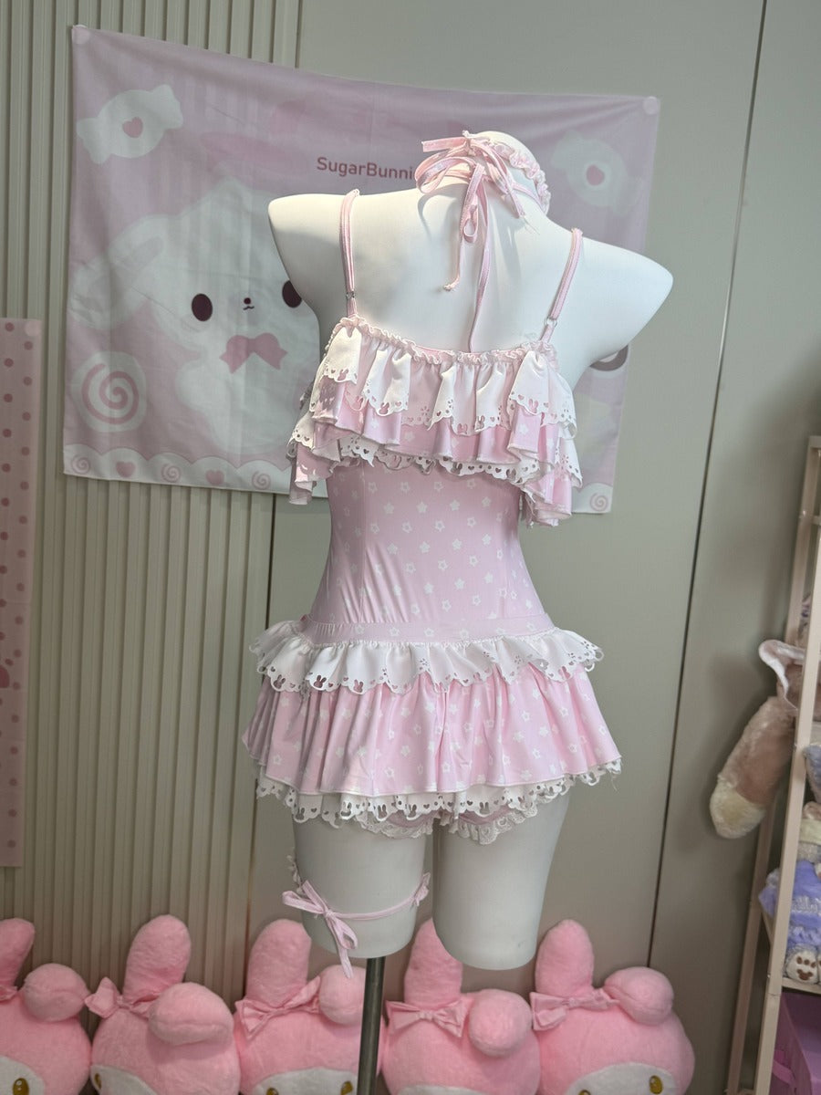 A pink and white polka dot halter neck one-piece swimsuit with ruffled trim, displayed on a white mannequin torso. The swimsuit features a halter top with a bow, a ruffled chest strap, and a tiered ruffled skirt with white lace trim.