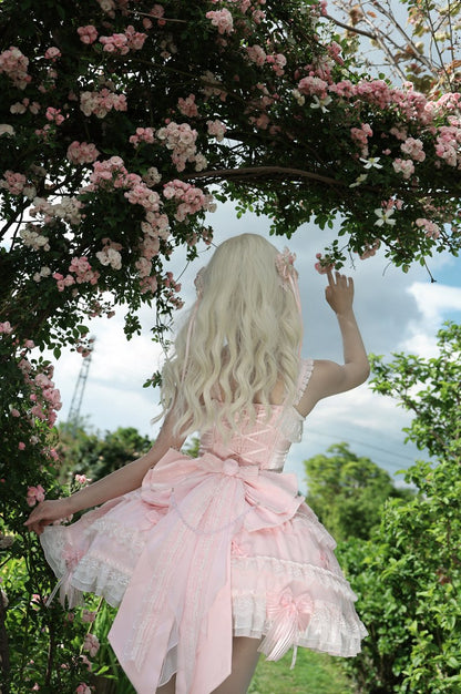 Woman in a pink dress standing under a canopy of pink flowers with a blue sky in the background