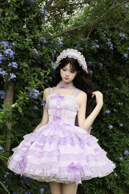 Woman in a lavender dress with ruffles standing in a garden with flowers and trees.