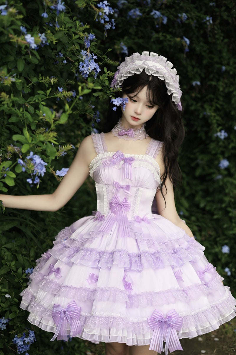 Woman in a lavender dress with ruffles and bows standing in front of green foliage.