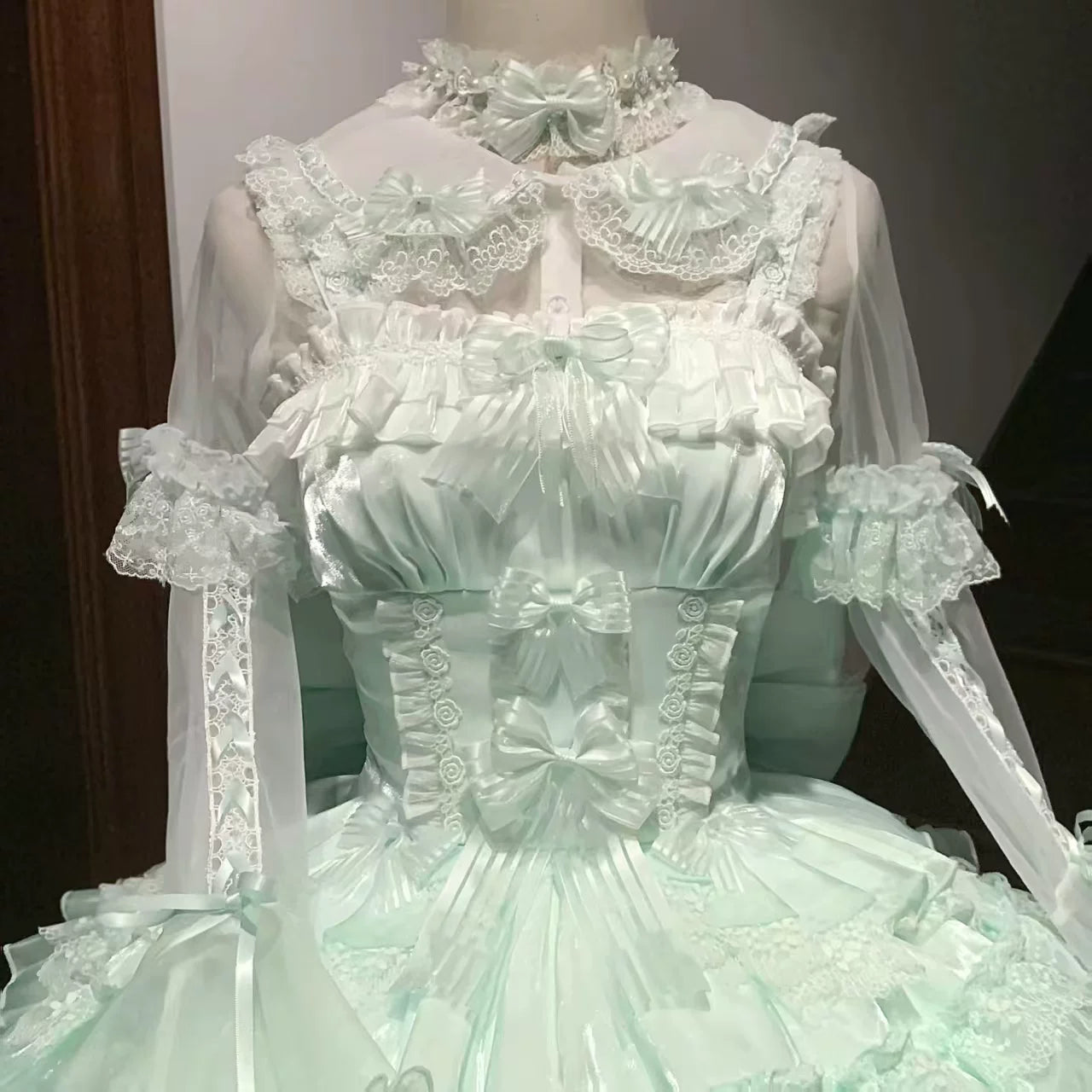 Detailed green dress with lace and bow accents on a mannequin.