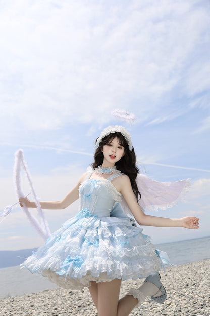 Woman in a light blue dress with angel wings standing on a beach.
