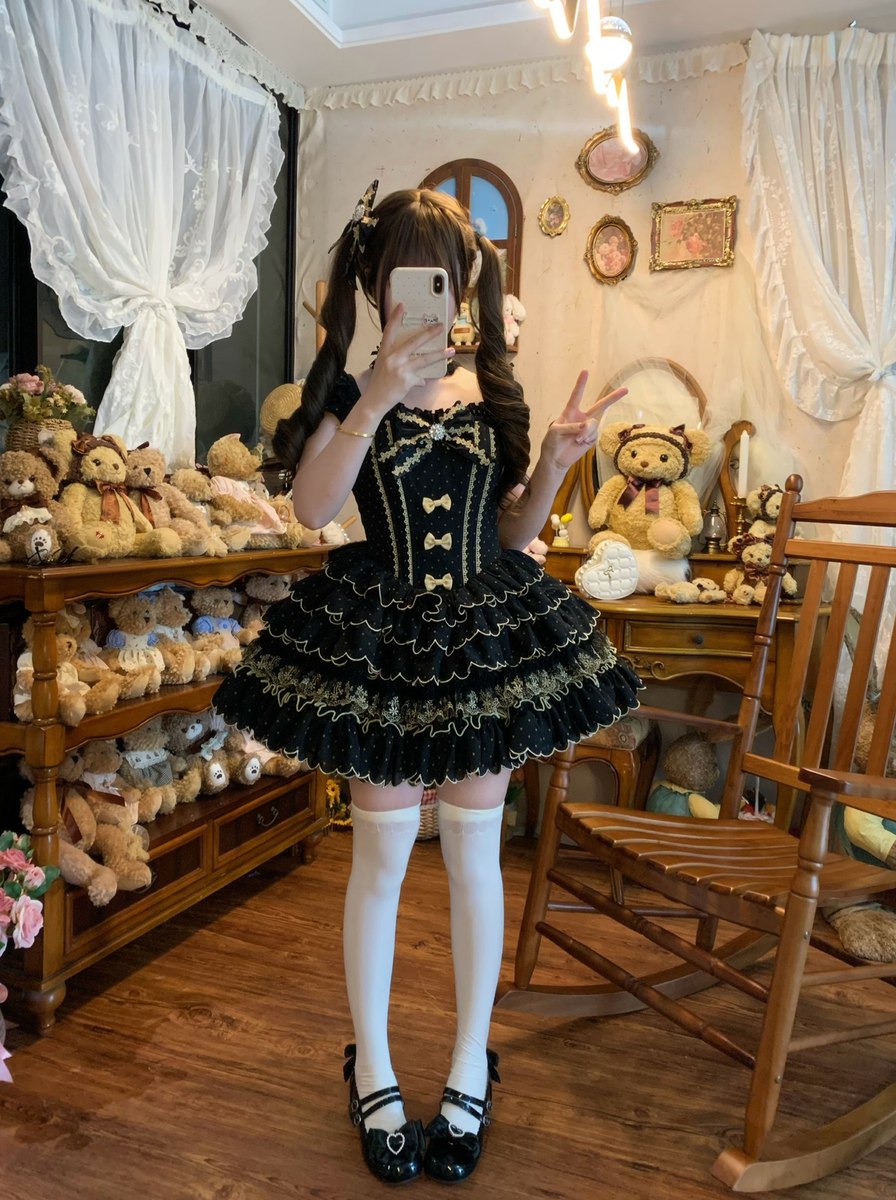 Person in a black and gold dress taking a selfie in a room with teddy bears and wooden furniture.