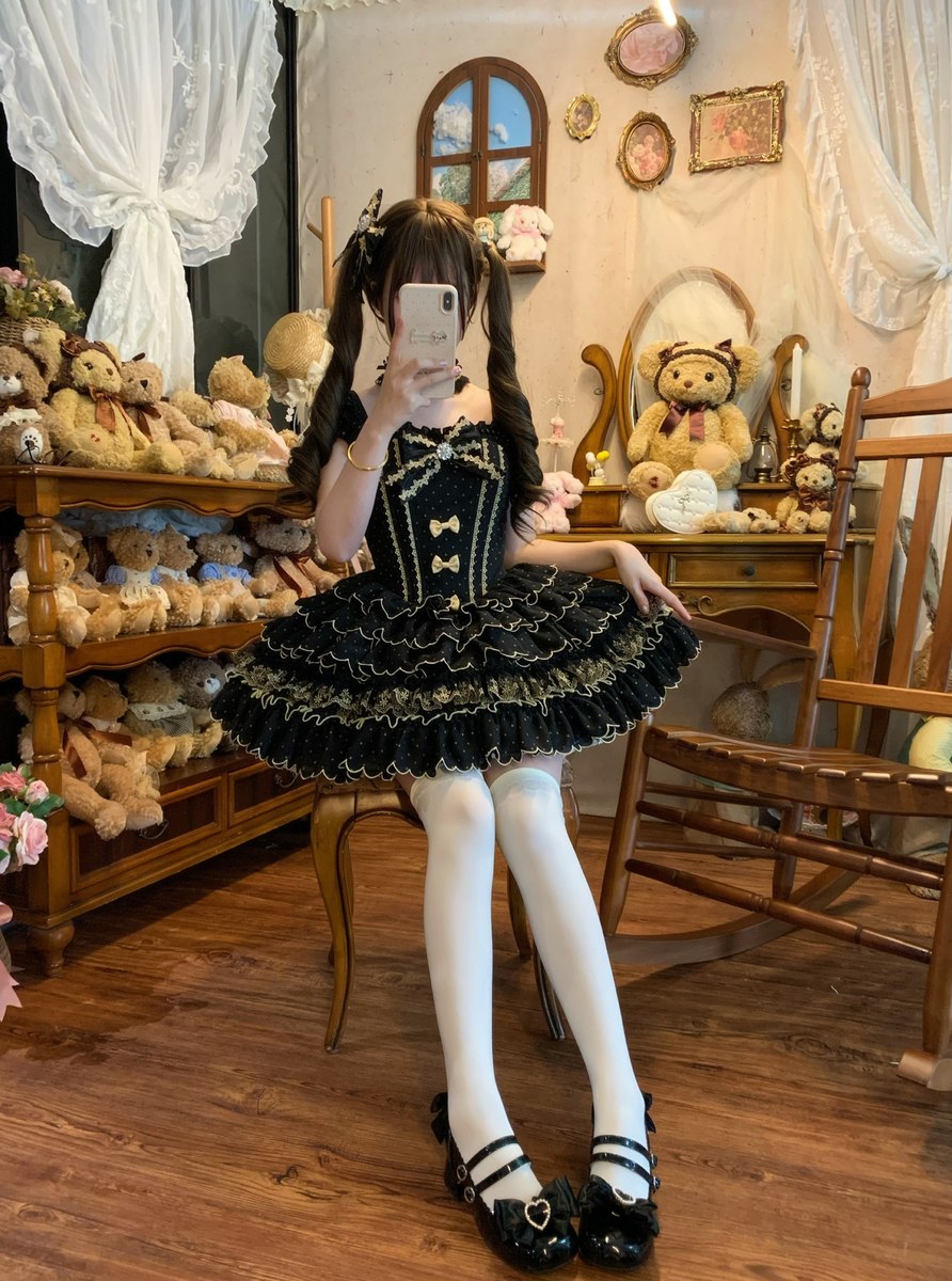 Person in a black and gold dress taking a mirror selfie in a room with teddy bears and decorative items.