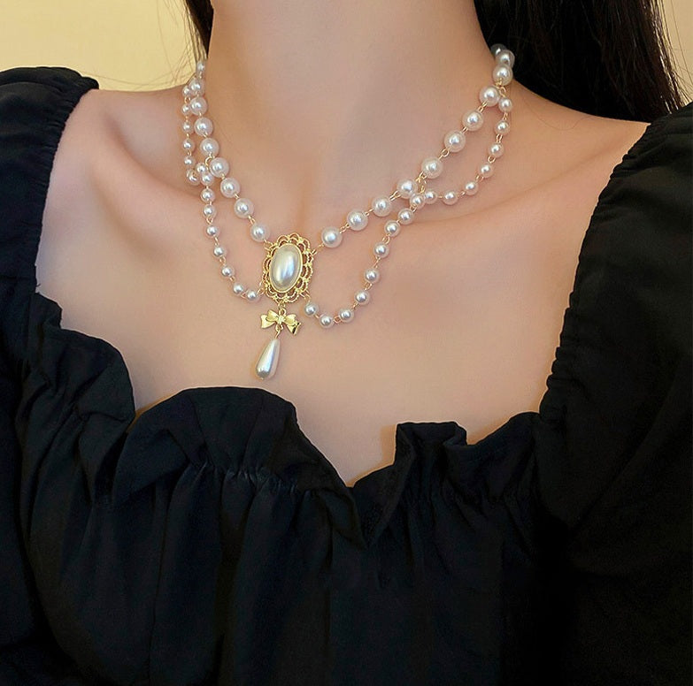 Pearl necklace with a gold pendant on a person wearing a black top.