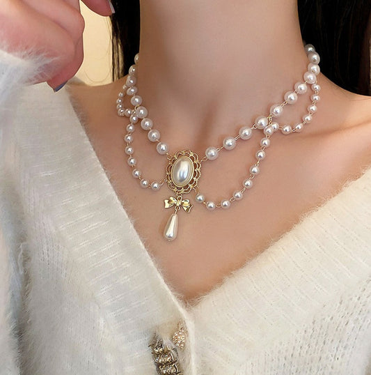 Pearl necklace with a decorative clasp worn by a person in a white outfit.
